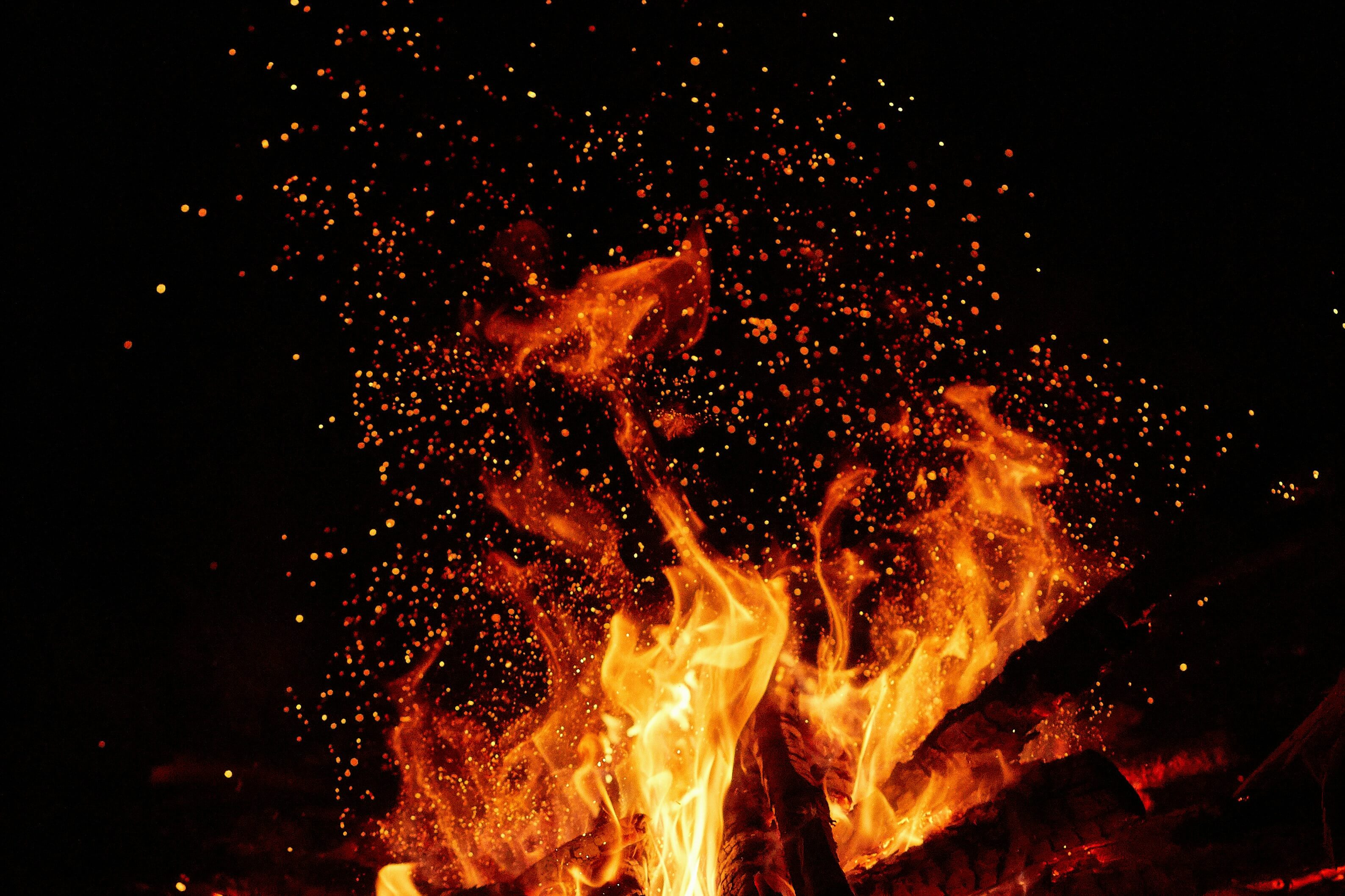 Close-up of bright orange and yellow flames with glowing embers against a dark background.