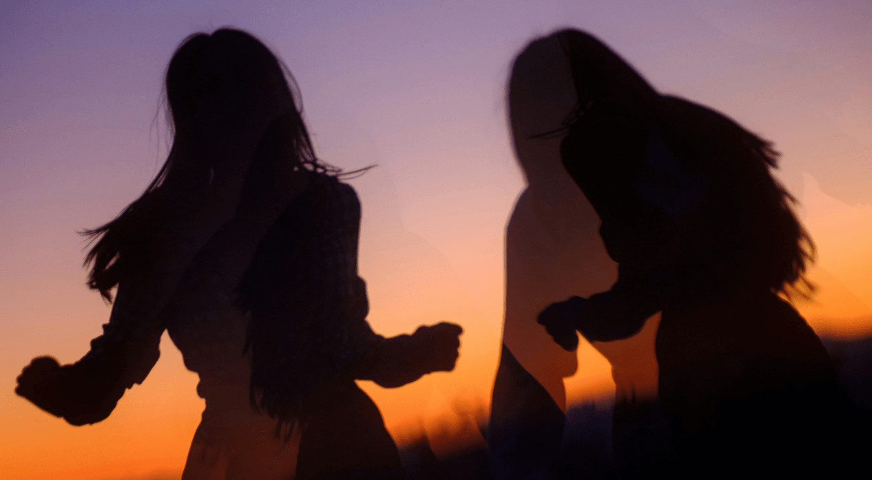 Silhouettes of two women dancing against a purple and orange sunset.