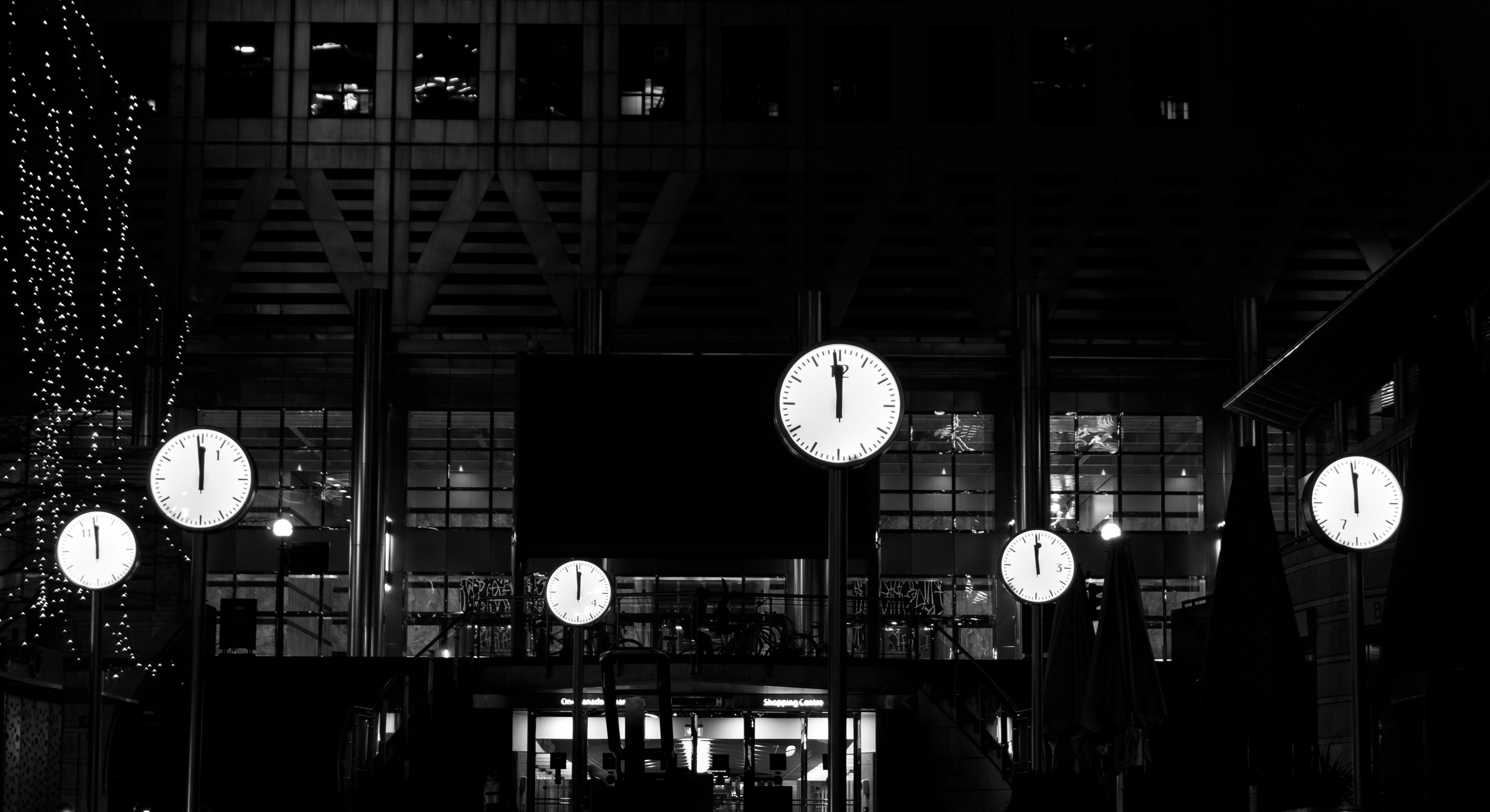 Five illuminated clocks on poles in front of a building at night.