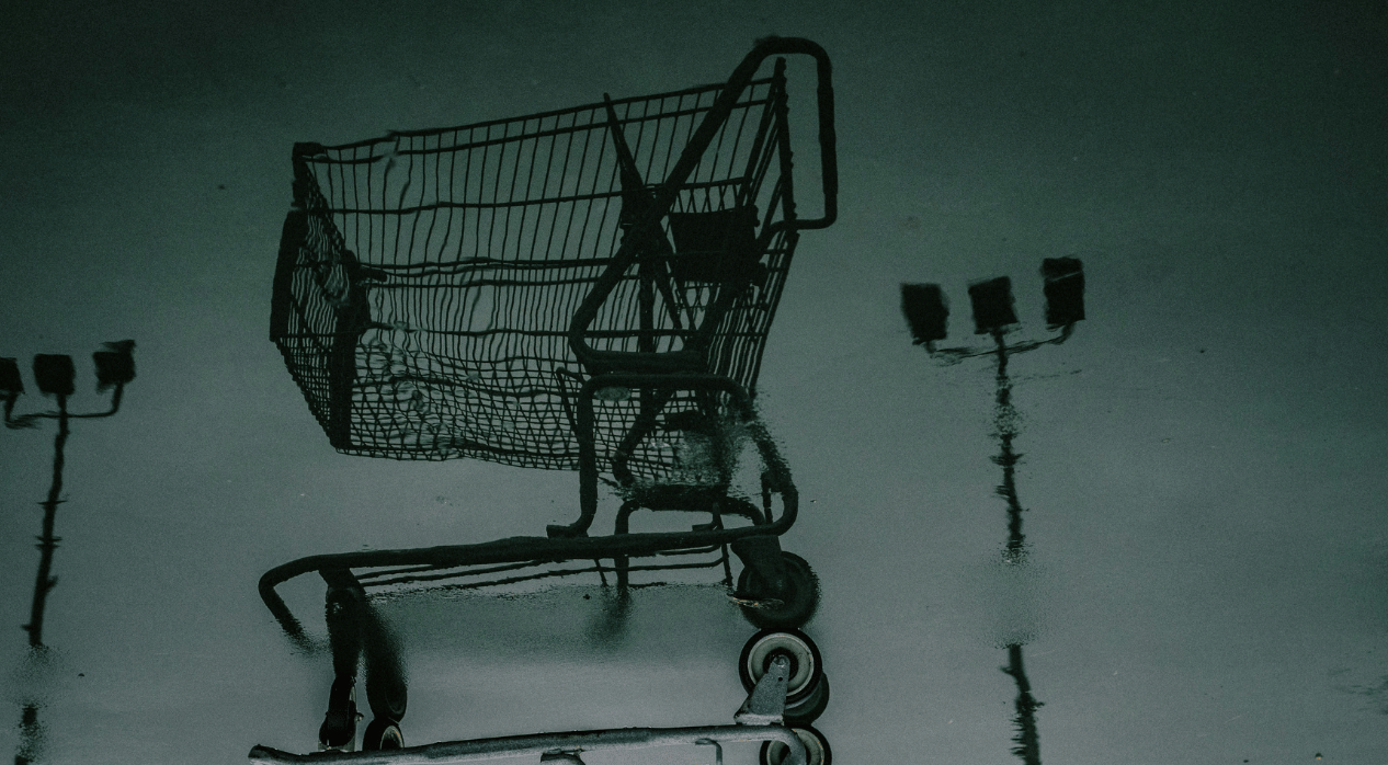 Reflection of a shopping cart and street lamps in a puddle on a dark surface.