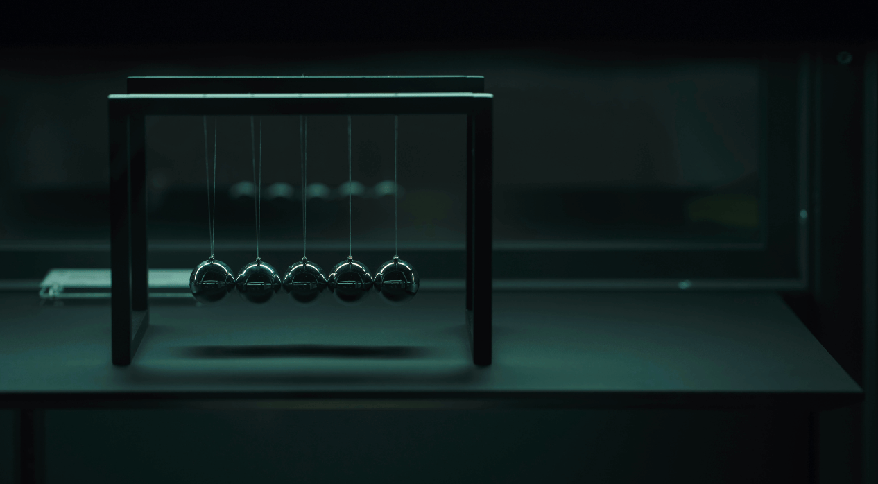 Newton's cradle with five metallic spheres on a flat surface in dim, greenish lighting.