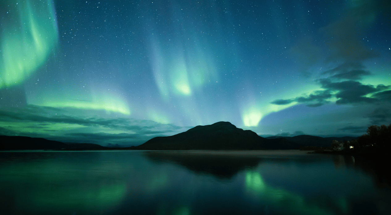 Northern Lights over a mountain with reflections on a water surface.