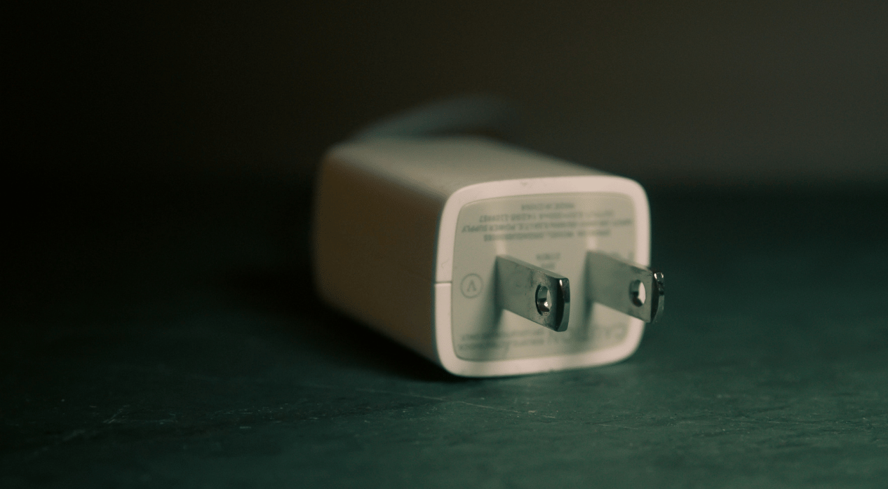 Close-up of a white USB wall charger on a dark surface with visible prongs.