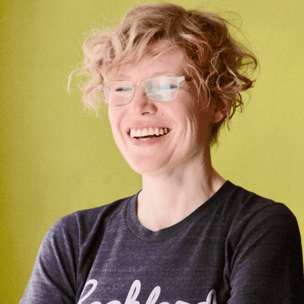 A person with curly hair wearing a dark gray t-shirt that reads "lockford" stands against a vibrant green backdrop.