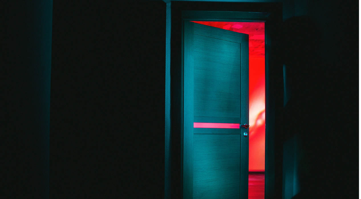 An open door with red light behind it in a dark room.