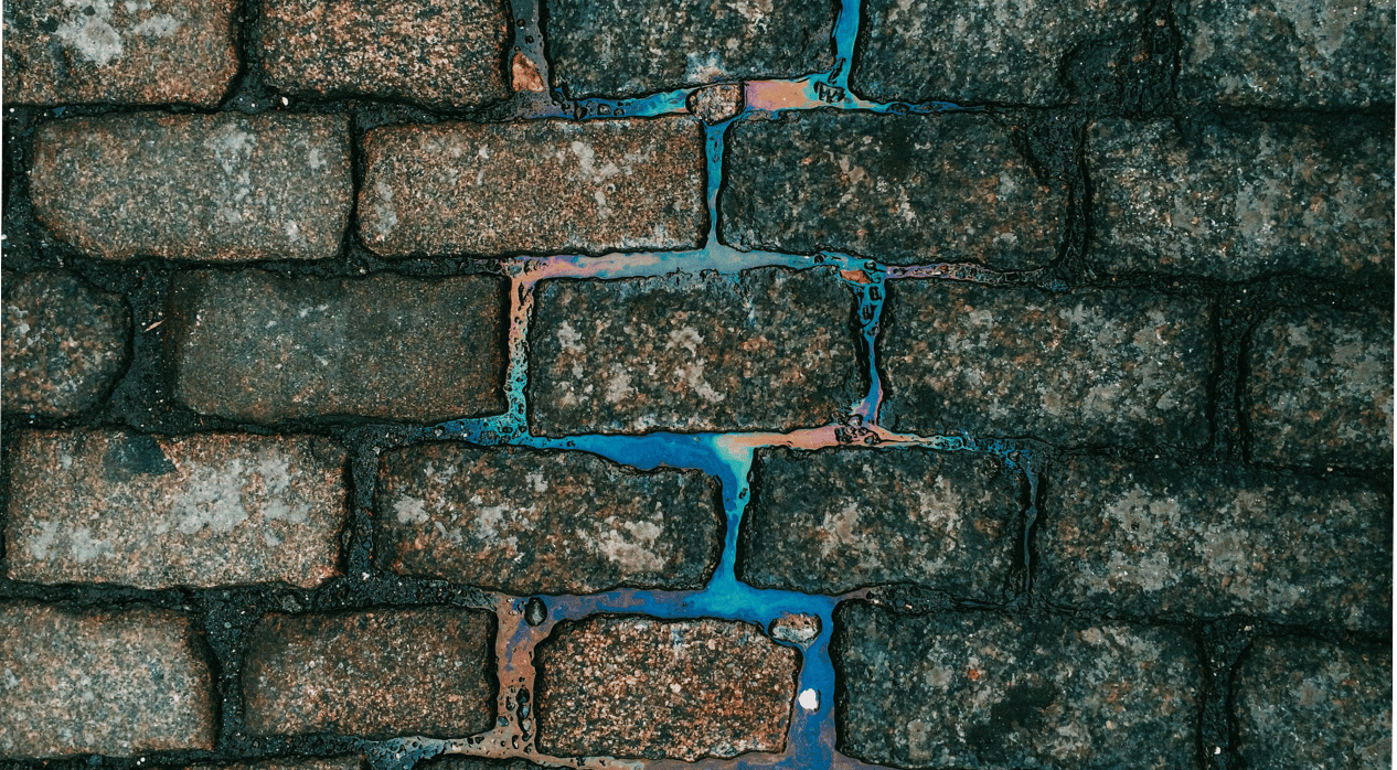 Cobblestone pavement with iridescent liquid between the stones.