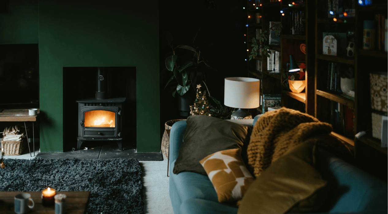 Cozy living room with a wood stove, teal sofa, bookshelves, and festive decor.