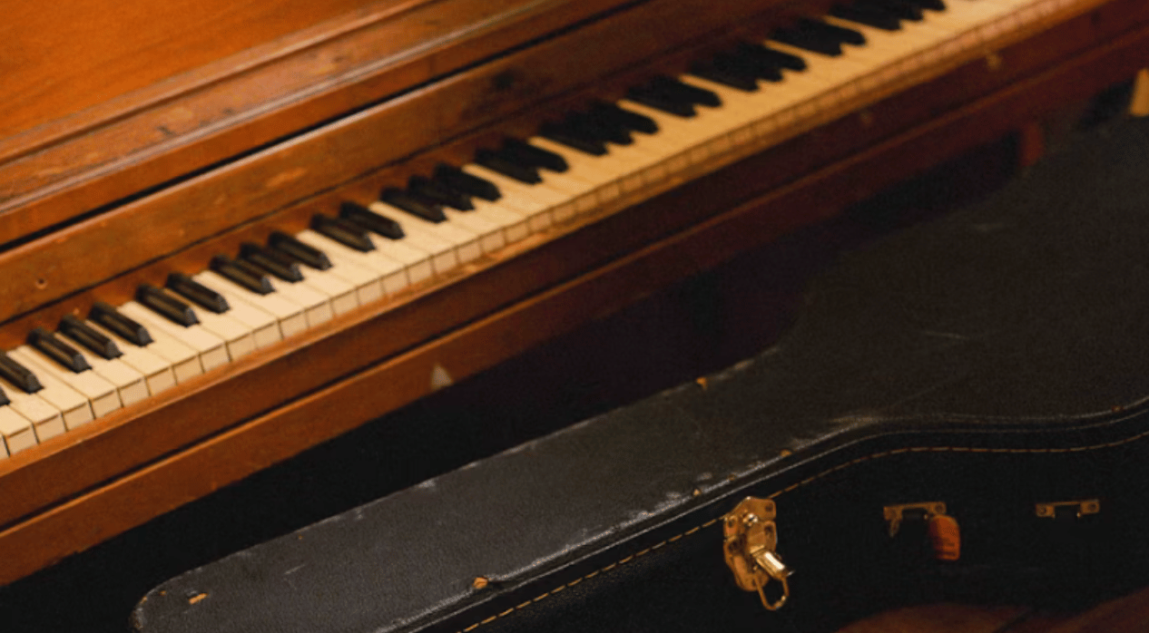 A black guitar case sits atop the bench of an oak piano