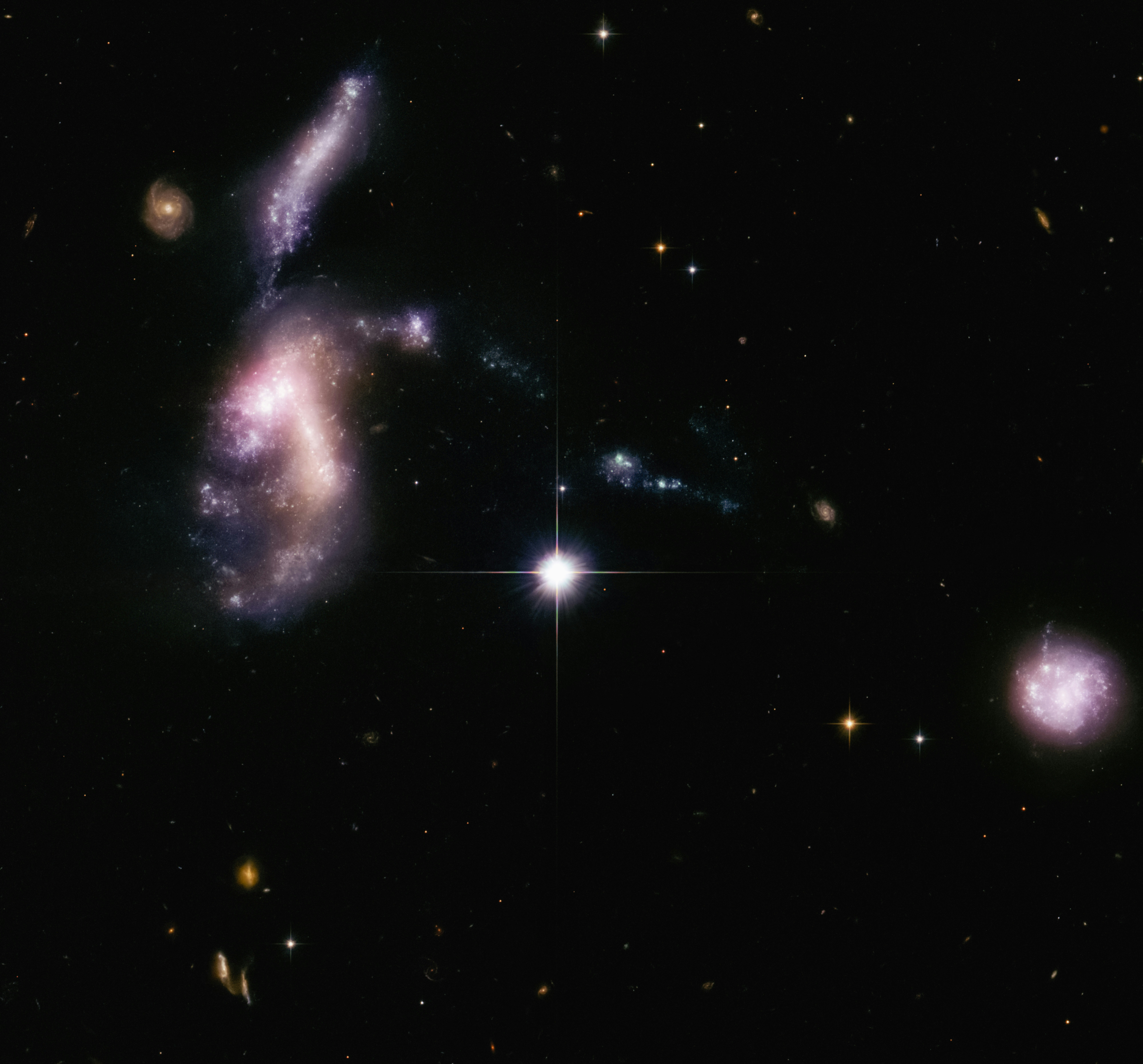 Four dwarf galaxies, purple, pink, and blue sit in a row in deep space.
