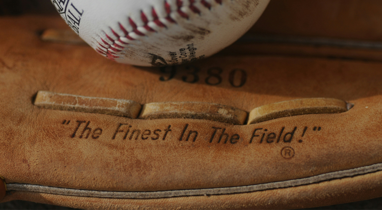 a worn baseball sitting in a brown baseball mitt with the words, "The finest on the field," etched into leather.